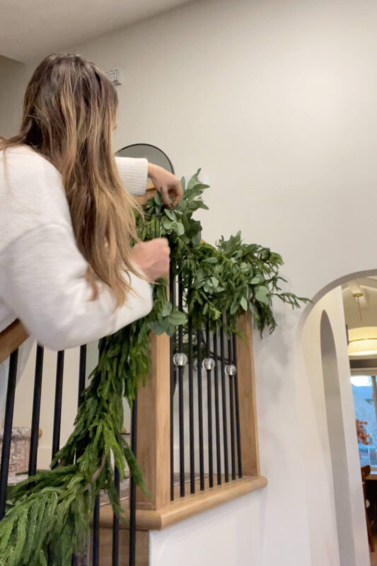 Adding faux eucalyptus garland to a double layer of pine garland.